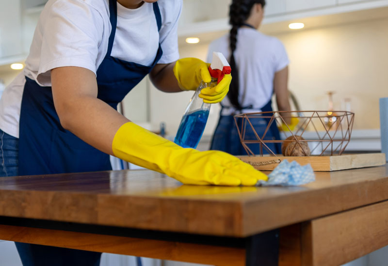 women cleaning a wooden table in a home