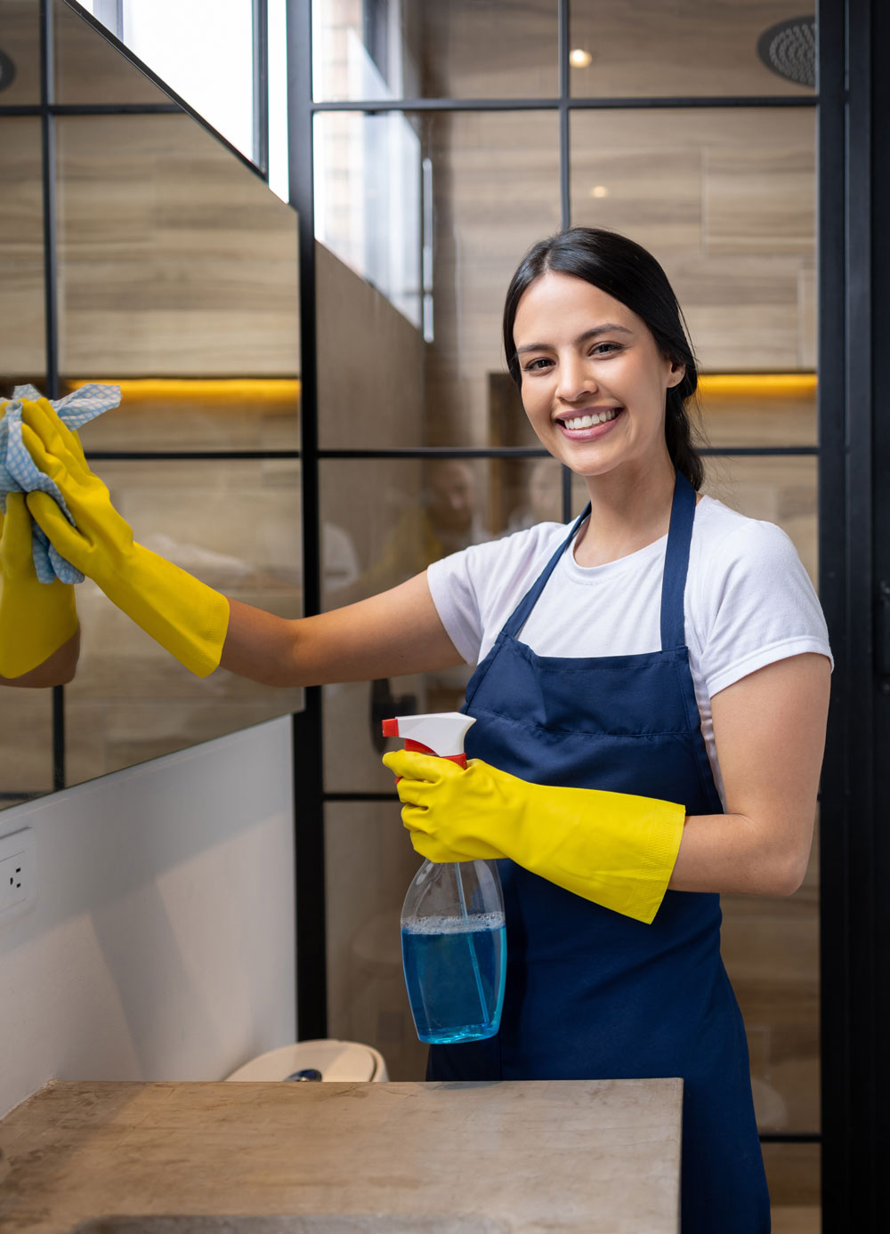 Cleaning Lady smiling and cleaning a bathroom mirror